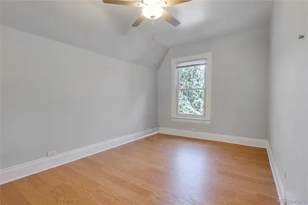 an empty room with wooden floor chandelier fan and windows