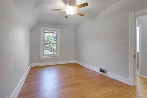an empty room with wooden floor chandelier fan and windows