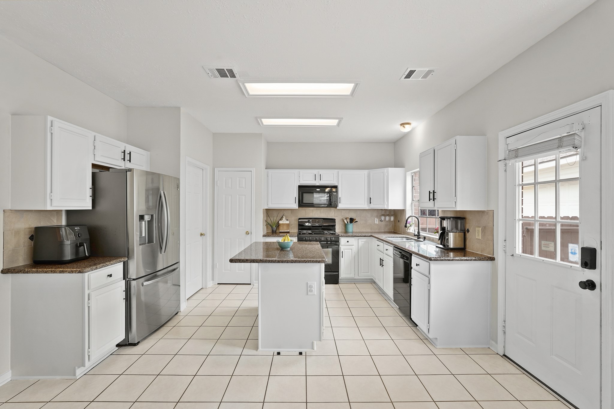 16114 Kintyre Point Road Houston, TX 77095 - Photo 18 of 44 Bright and spacious kitchen with modern appliances, white cabinets, and a central island. Features include tiled floors, ample natural light, and a door leading outside.