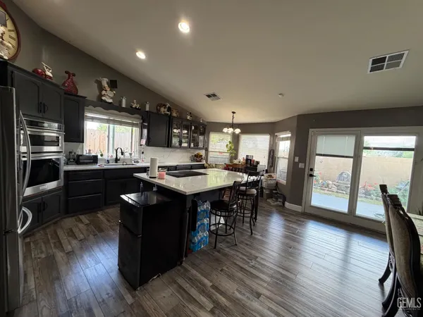 a kitchen with stainless steel appliances granite countertop a refrigerator a stove a sink dishwasher and a dining table with wooden floor