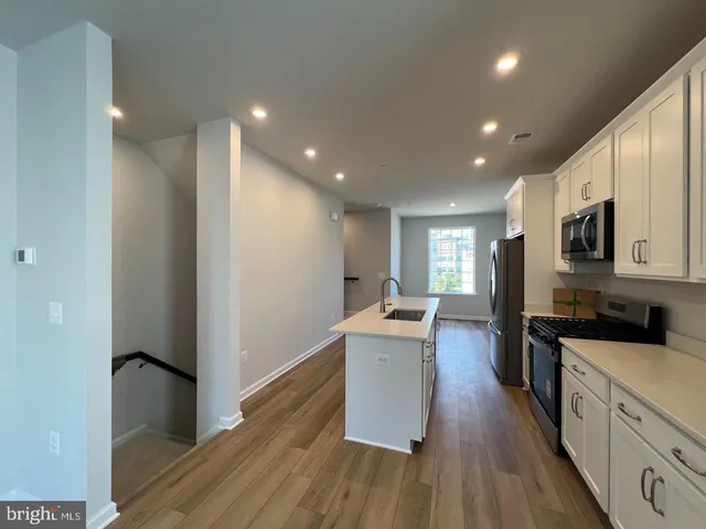 a kitchen with stainless steel appliances granite countertop a refrigerator a sink dishwasher a stove and white countertops with wooden floor