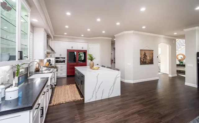 a kitchen with stainless steel appliances granite countertop a stove top oven a sink dishwasher a dining table and chairs with wooden floor