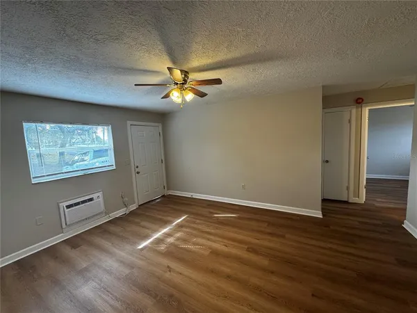an empty room with wooden floor chandelier fan and windows