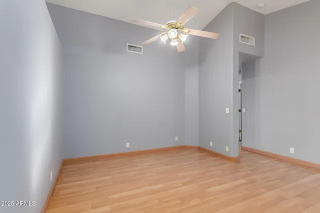 an empty room with a chandelier fan and wooden floor