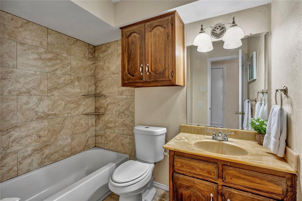 108 Prairie Creek Road Red Oak, TX 75154 - Photo 10 of 19 Bathroom featuring a full tub with tiled surround, a corner vanity with an integrated sink, and an overhead wooden storage cabinet