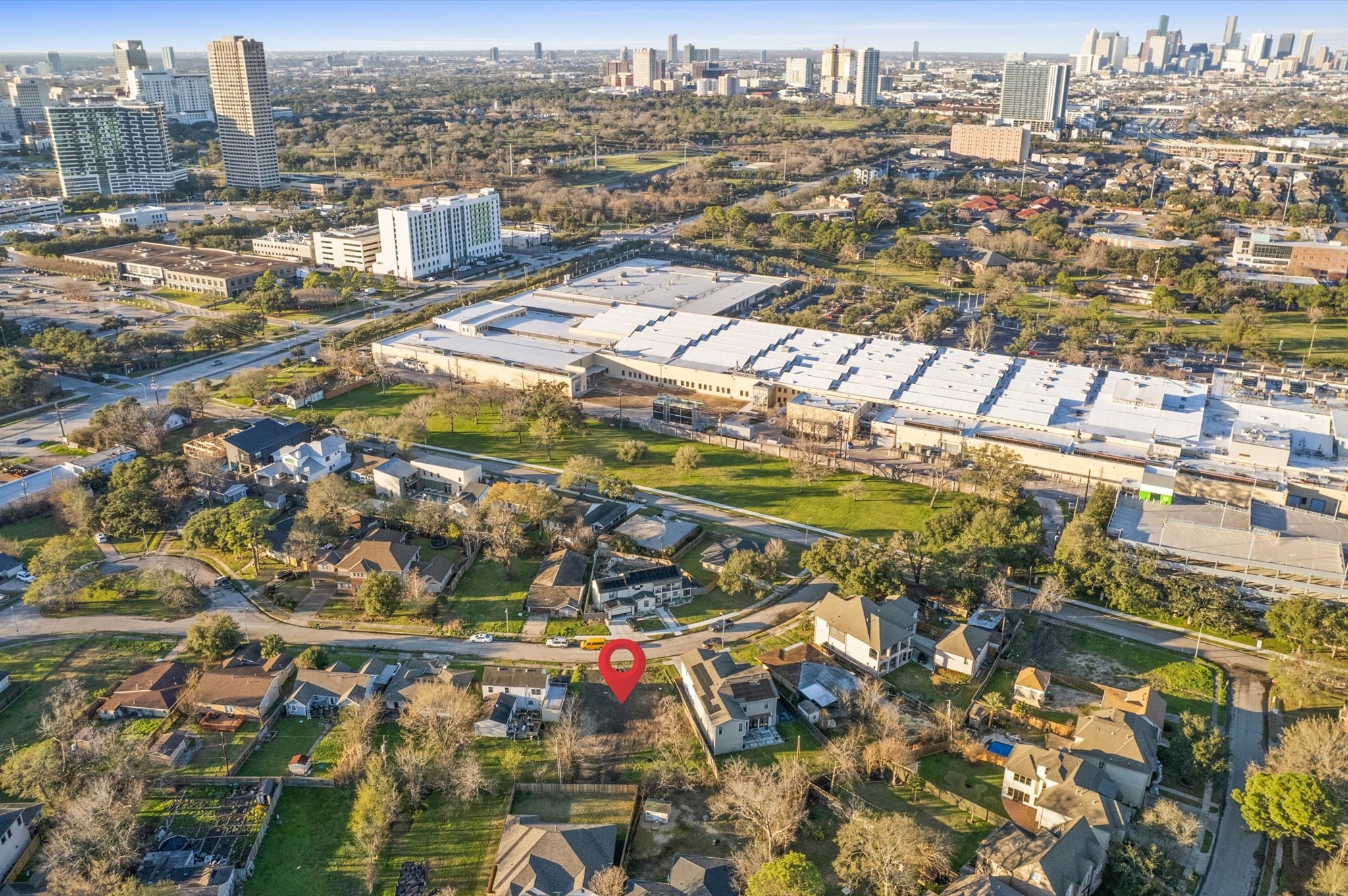 6919 Burgess Street Houston, TX 77021 - Photo 3 of 12 This aerial photo showcases a residential neighborhood with a mix of houses surrounded by greenery. The area is near a large commercial building and urban skyline, indicating proximity to city amenities and business centers.