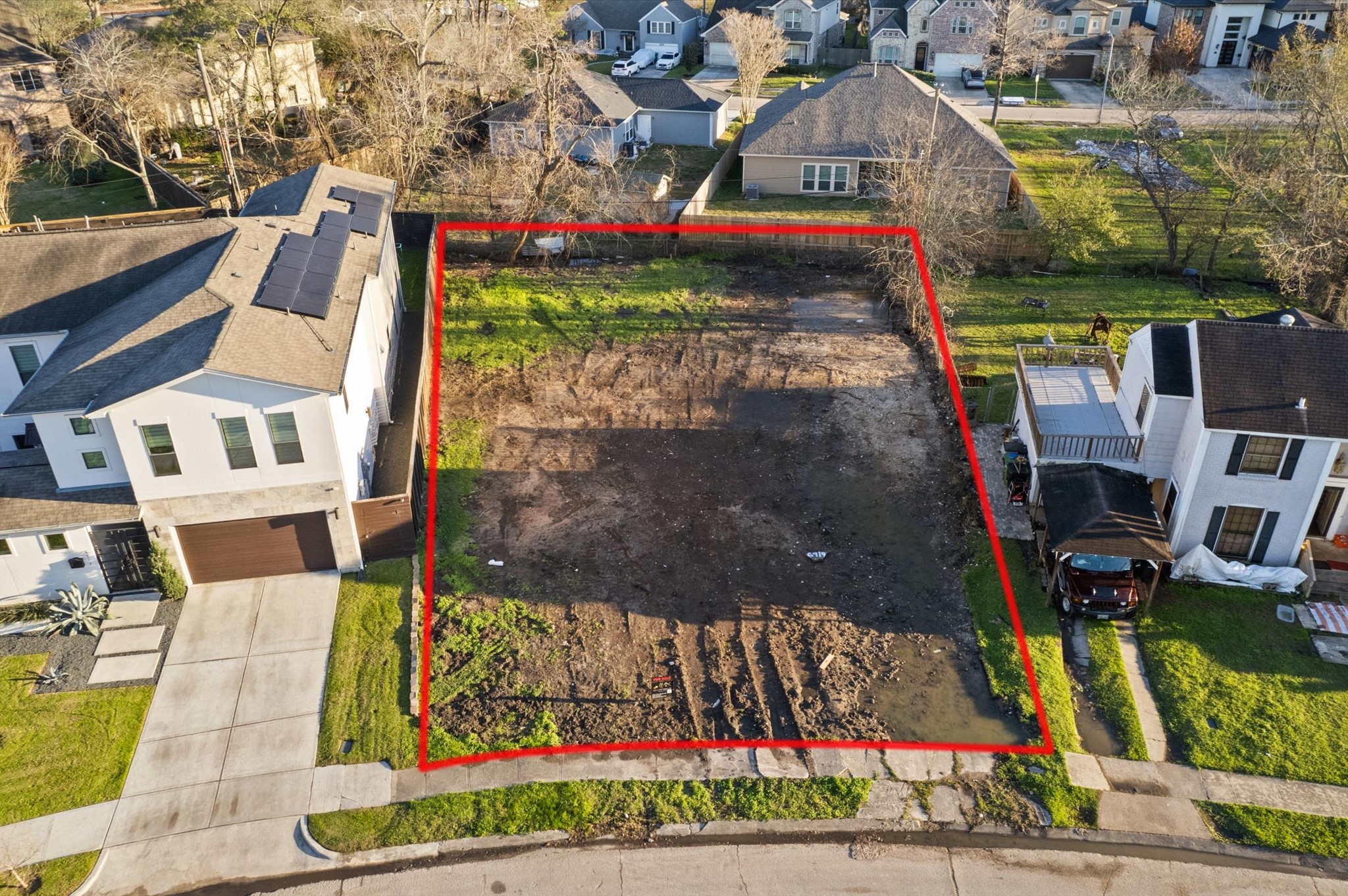 6919 Burgess Street Houston, TX 77021 - Photo 5 of 12 This photo shows a vacant lot outlined in red, situated between two modern homes in a residential neighborhood. The land appears cleared and ready for construction, with a driveway entrance and neighboring houses visible.