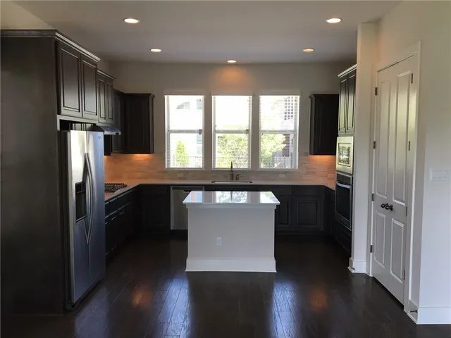 a kitchen with stainless steel appliances granite countertop a refrigerator a sink dishwasher a stove and a refrigerator with wooden floor