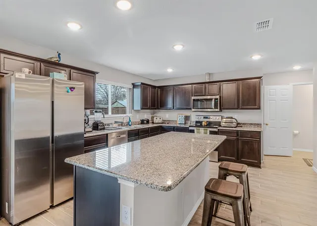 a kitchen with a refrigerator a sink a stove a dining table and chairs