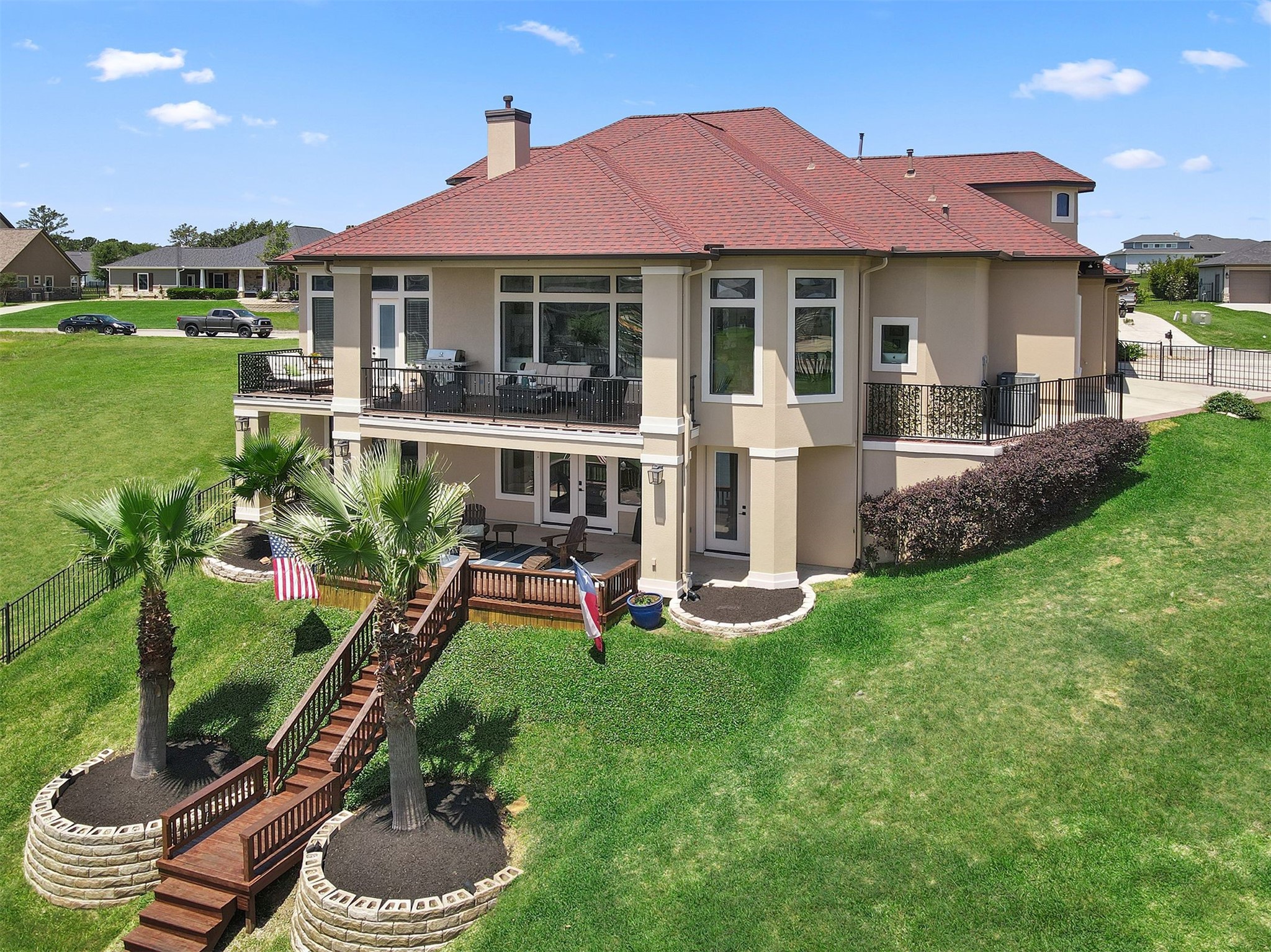 10896 Decatur Street Willis, TX 77318 - Photo 5 of 50 This stunning modern home boasts expansive glass windows, a spacious two-level deck, and a beautifully landscaped yard with palm trees, offering ample outdoor space and scenic views perfect for enjoying the outdoors.
