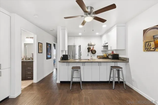 a kitchen with stainless steel appliances a refrigerator a sink dishwasher and white cabinets with wooden floor