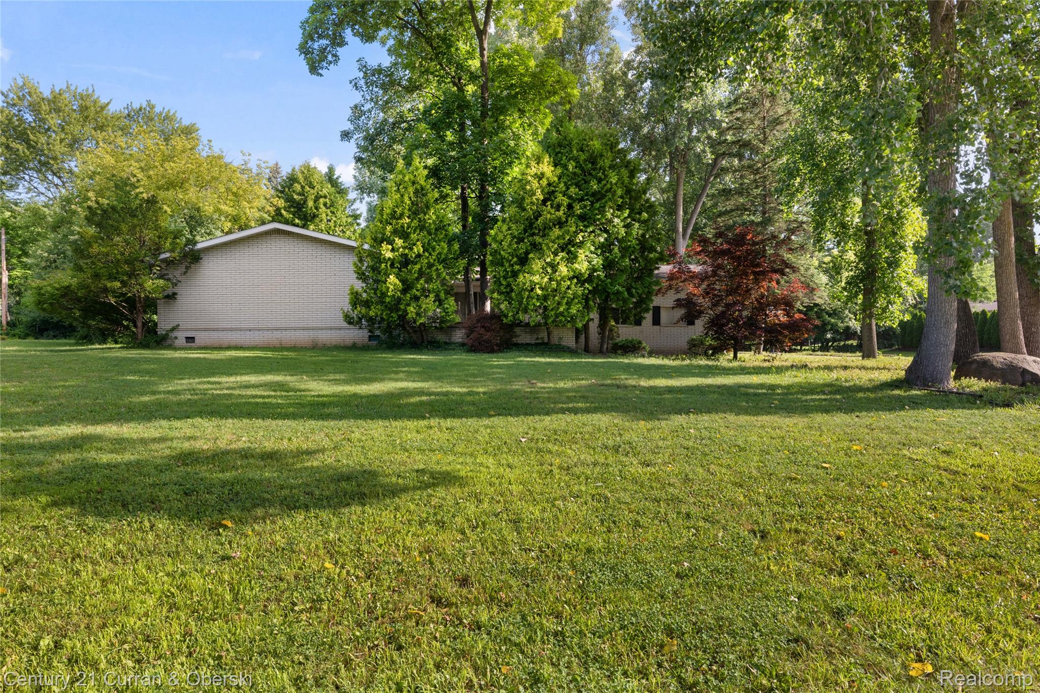 4652 Patrick Road West Bloomfield, MI 48322 - Photo 20 of 27 Expansive green lawn surrounded by mature trees, featuring a light-colored brick exterior on the property structure