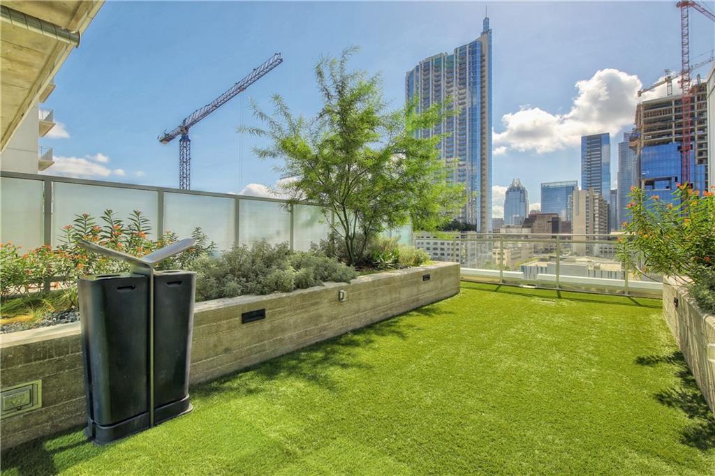 222 West Avenue, Unit 2207 Austin, TX 78701 - Photo 30 of 30 Rooftop terrace with artificial turf, concrete planters featuring mature landscaping, and a clear panel railing system