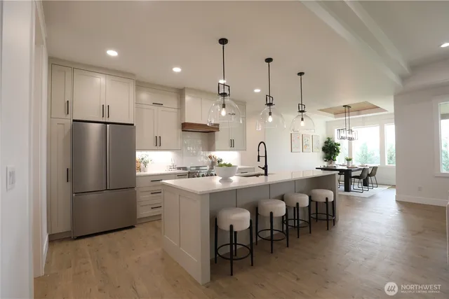 a kitchen with stainless steel appliances kitchen island granite countertop a dining table chairs refrigerator sink and cabinets