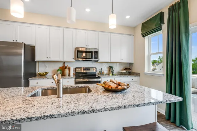 a kitchen with stainless steel appliances granite countertop a stove a sink a microwave a refrigerator and white cabinets with wooden floor