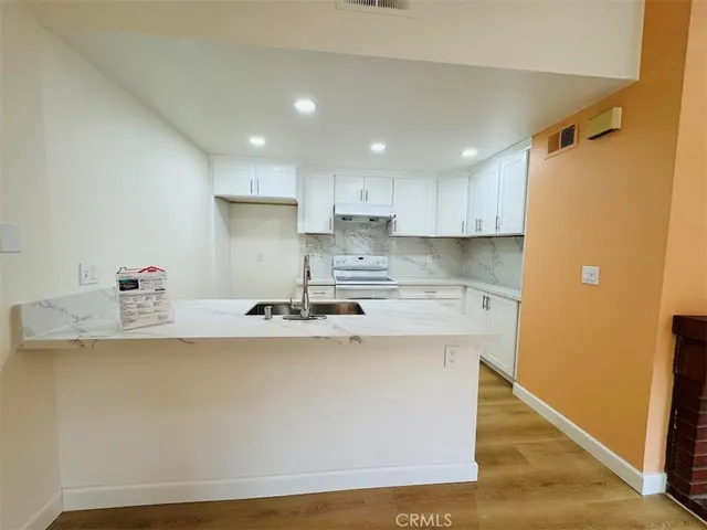 a kitchen with stainless steel appliances granite countertop a sink a stove a refrigerator and white cabinets