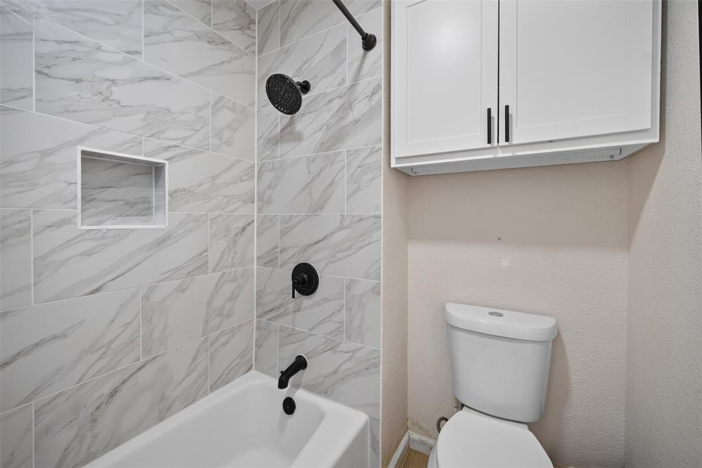 3919 Ridgeoak Way Farmers Branch, TX 75244 - Photo 19 of 28 Tub and shower with marbled tile surround, featuring matte black fixtures and a recessed niche
