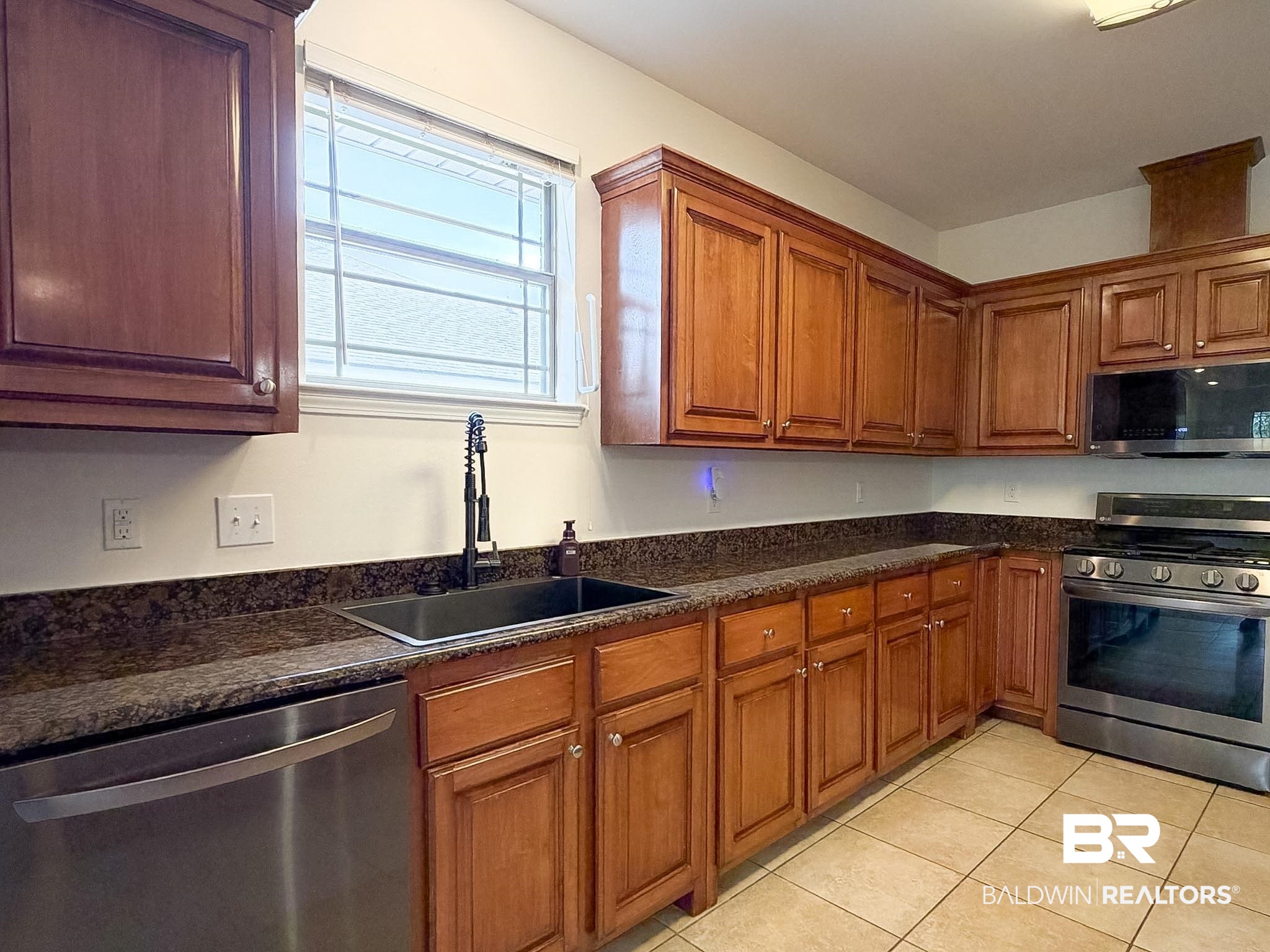 7332 Raintree Lane Gulf Shores, AL 36542 - Photo 7 of 21 Kitchen with stainless steel appliances, wood finish cabinetry, light tile patterned floors, and dark stone countertops