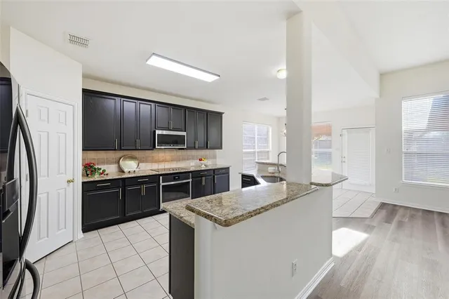a kitchen with stainless steel appliances kitchen island granite countertop a refrigerator a sink dishwasher a stove with wooden cabinets and floor