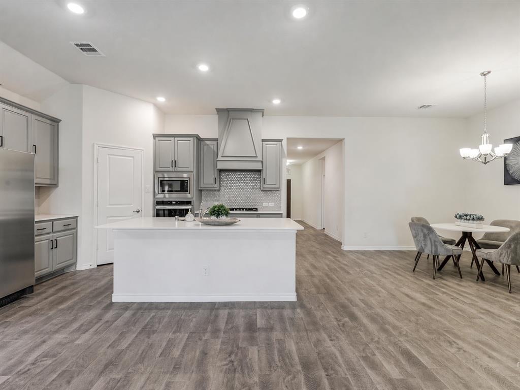 3024 Meredith Lane Forney, TX 75126 - Photo 9 of 29 Open-concept kitchen featuring an island, light gray cabinetry, stainless steel appliances, a tile backsplash, and wood-finish flooring