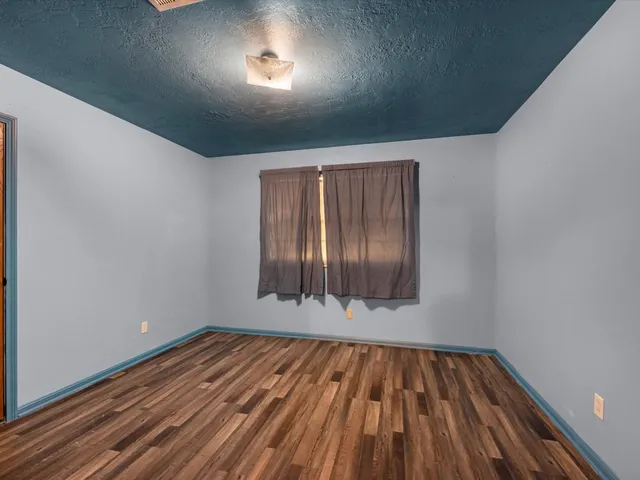 a view of an empty room with wooden floor and fan