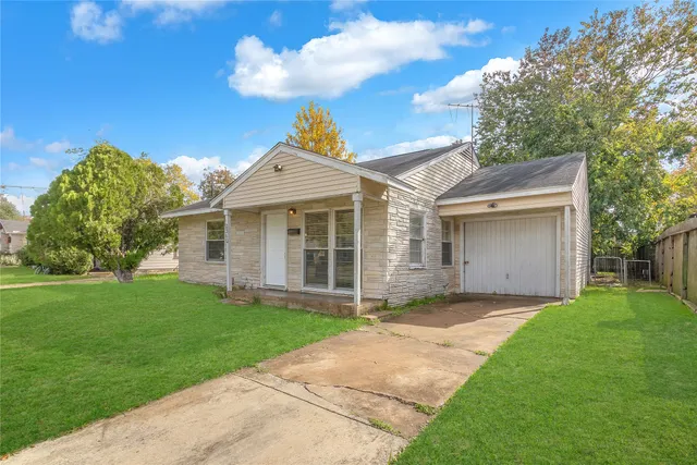 a view of a yard in front of a house with plants and large tree