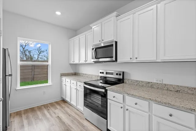 a kitchen with granite countertop white cabinets stainless steel appliances and a window