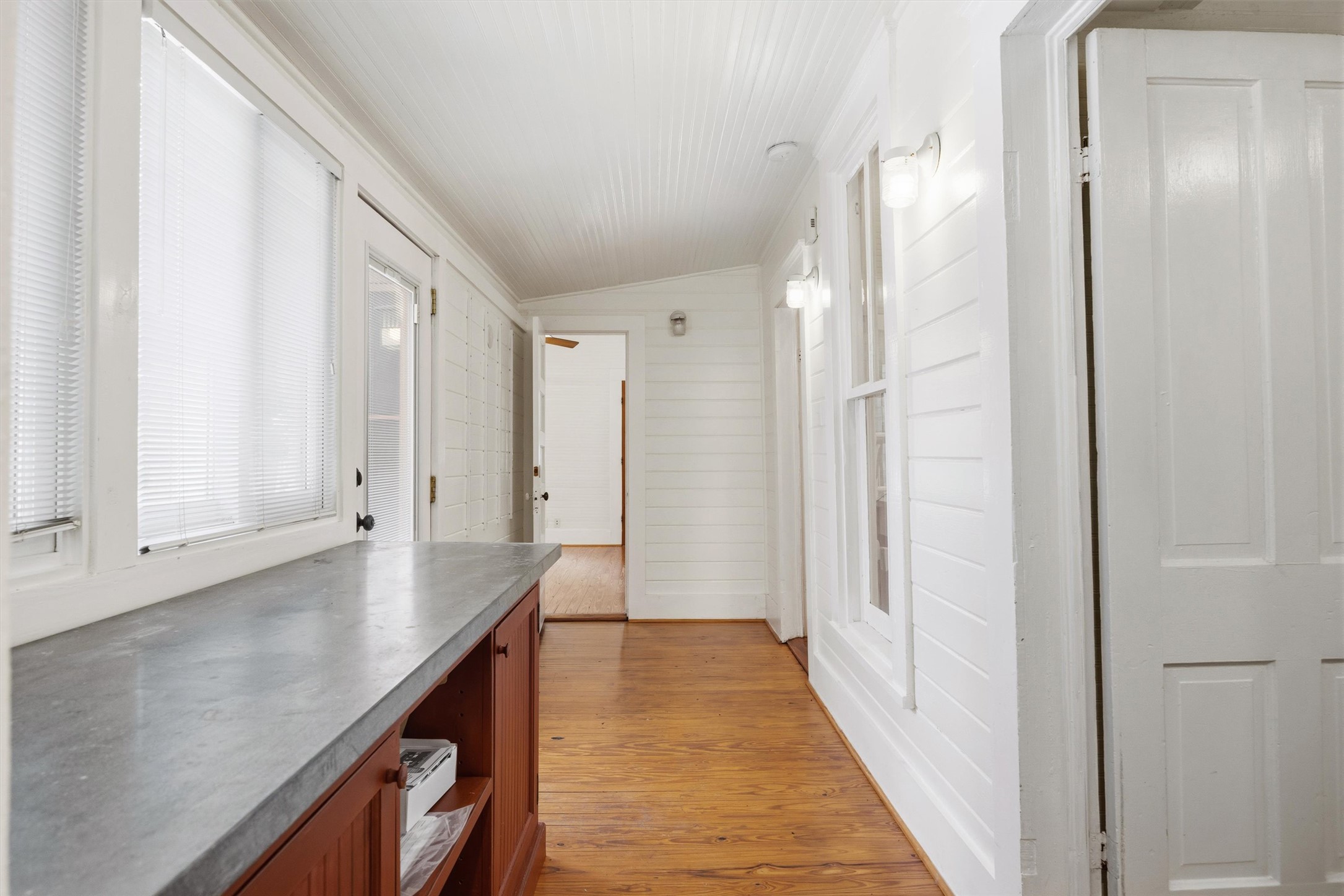 1613 Drake Avenue Austin, TX 78704 - Photo 11 of 27 Hallway featuring wood-finish flooring, white shiplap walls, multiple windows with blinds, a built-in wood cabinet with a solid surface countertop, and paneled doors