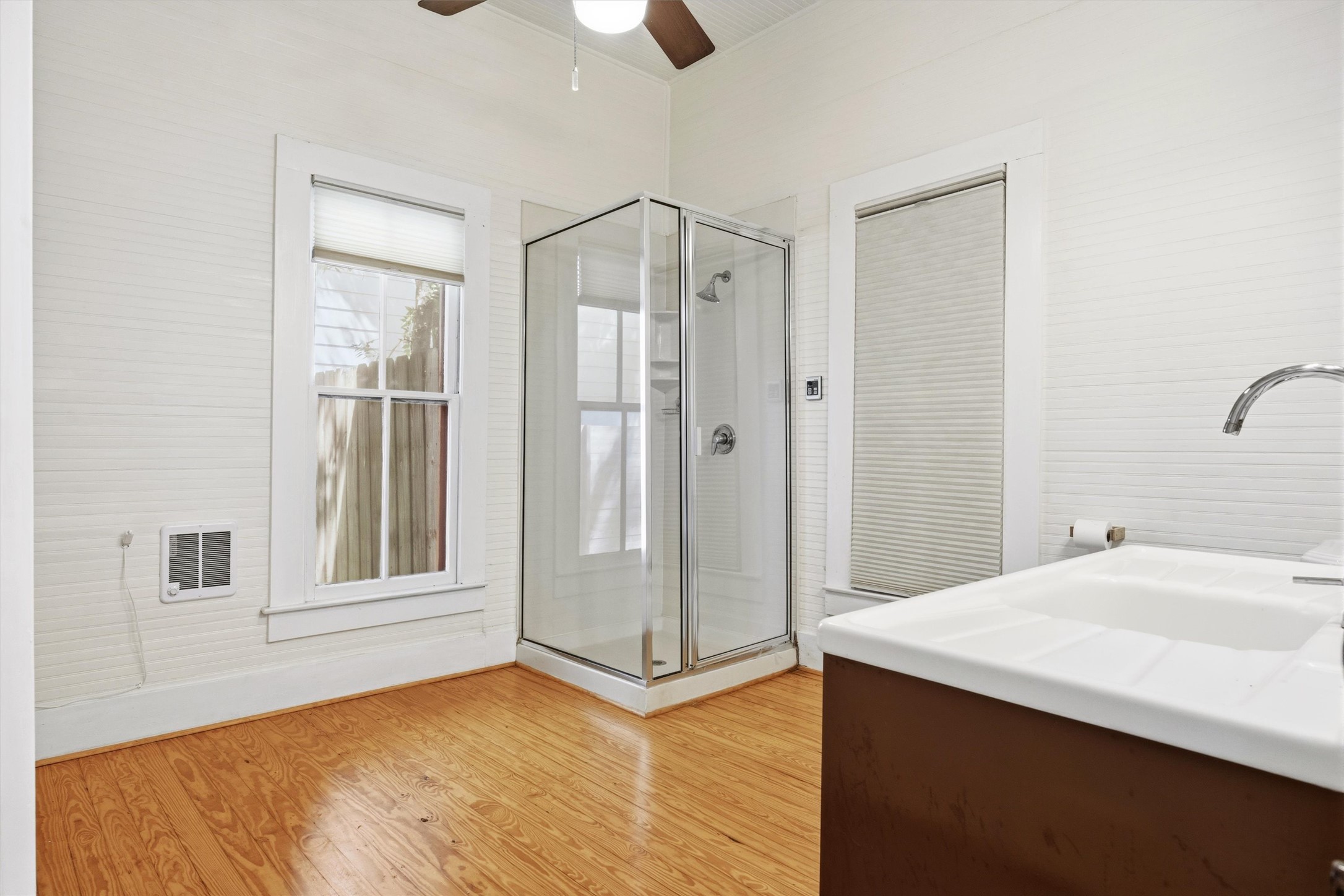 1613 Drake Avenue Austin, TX 78704 - Photo 12 of 27 Bathroom featuring a corner glass-enclosed shower, a double-basin vanity with a chrome faucet, light wood-finish flooring, and white horizontal paneling