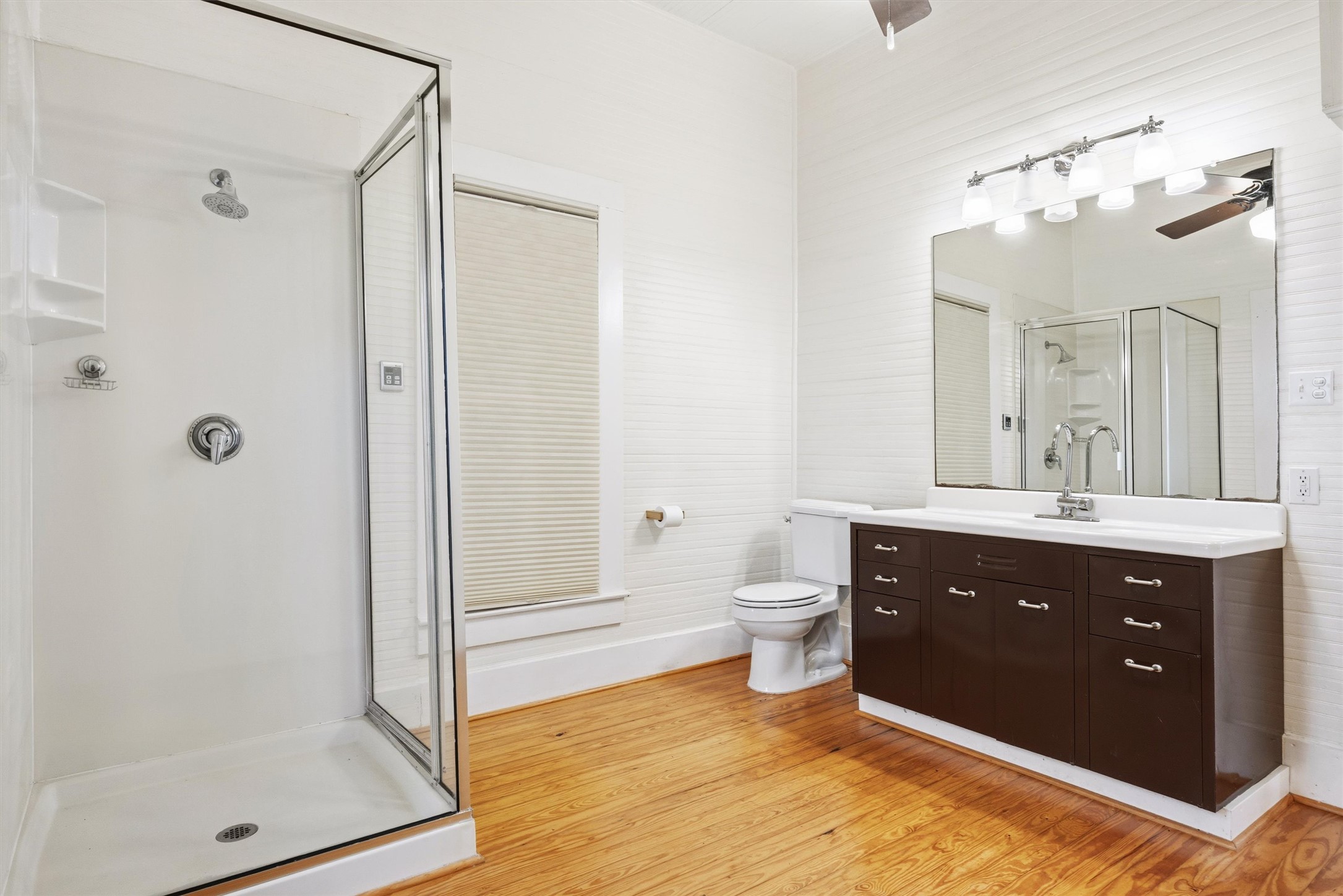 1613 Drake Avenue Austin, TX 78704 - Photo 13 of 27 Bathroom featuring a glass-enclosed shower, wood-finish flooring, a dark wood-finish vanity with a white countertop and integrated sink, a large mirror, and a ceiling fan