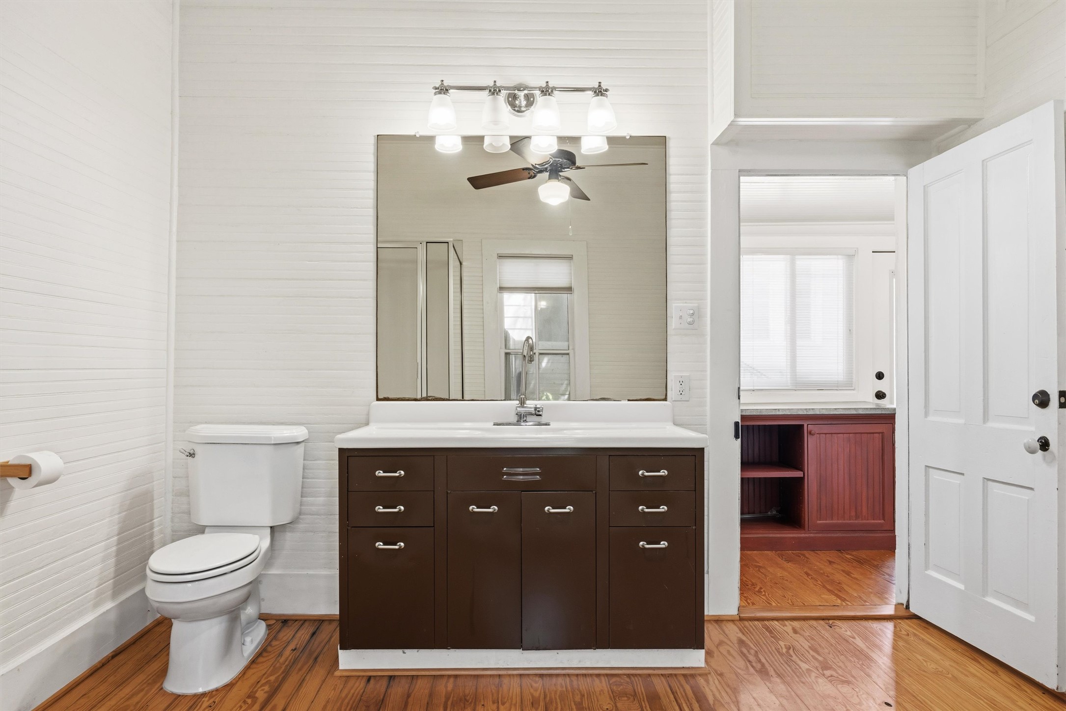 1613 Drake Avenue Austin, TX 78704 - Photo 14 of 27 Bathroom featuring shiplap walls, wood-finish flooring, a vanity with a white countertop, a toilet, and a large mirror with a four-light fixture