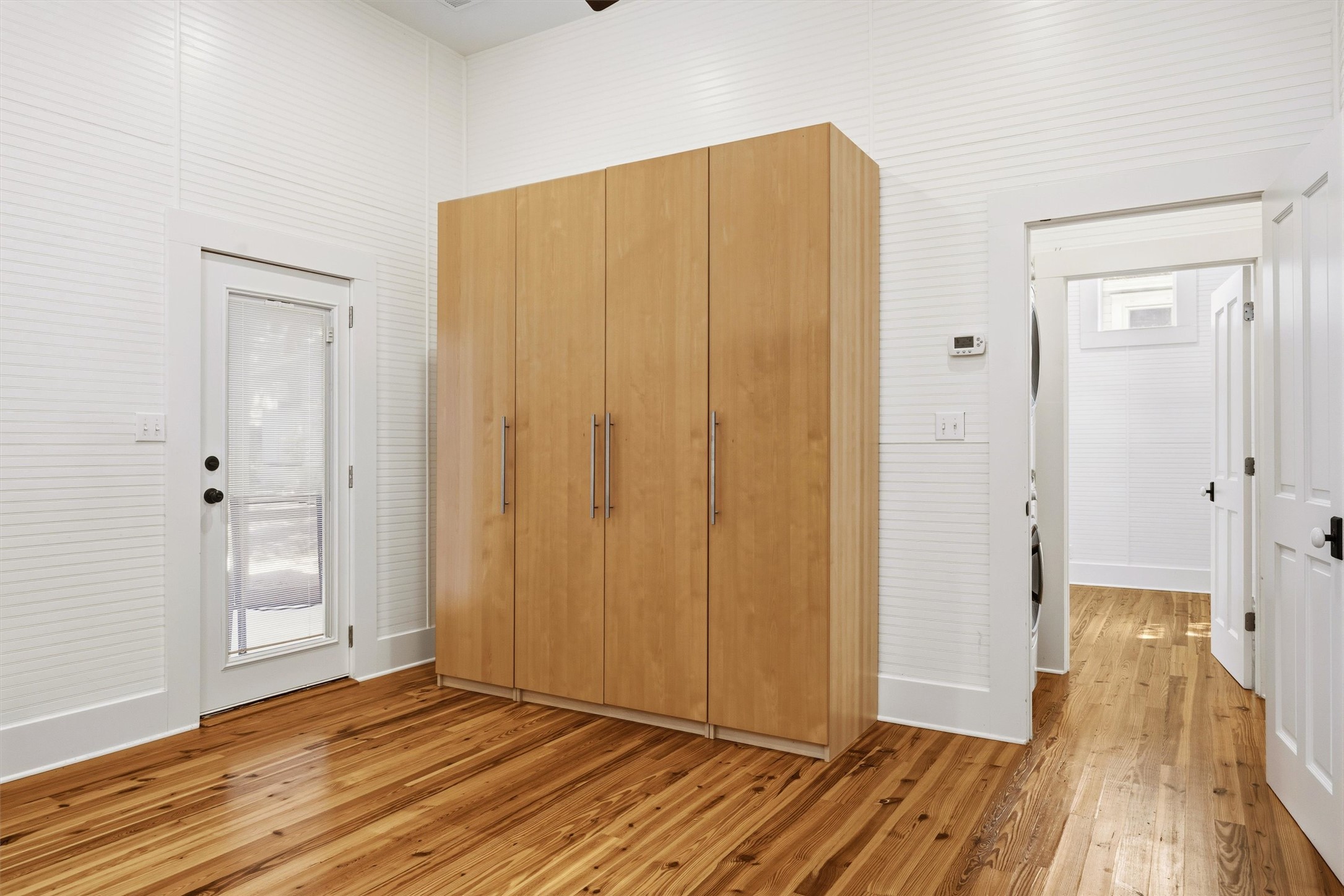1613 Drake Avenue Austin, TX 78704 - Photo 18 of 27 Spacious room featuring wood-finish flooring, white horizontal slat wall paneling, a full-lite exterior door, and a built-in light wood-finish storage cabinet with brushed nickel hardware