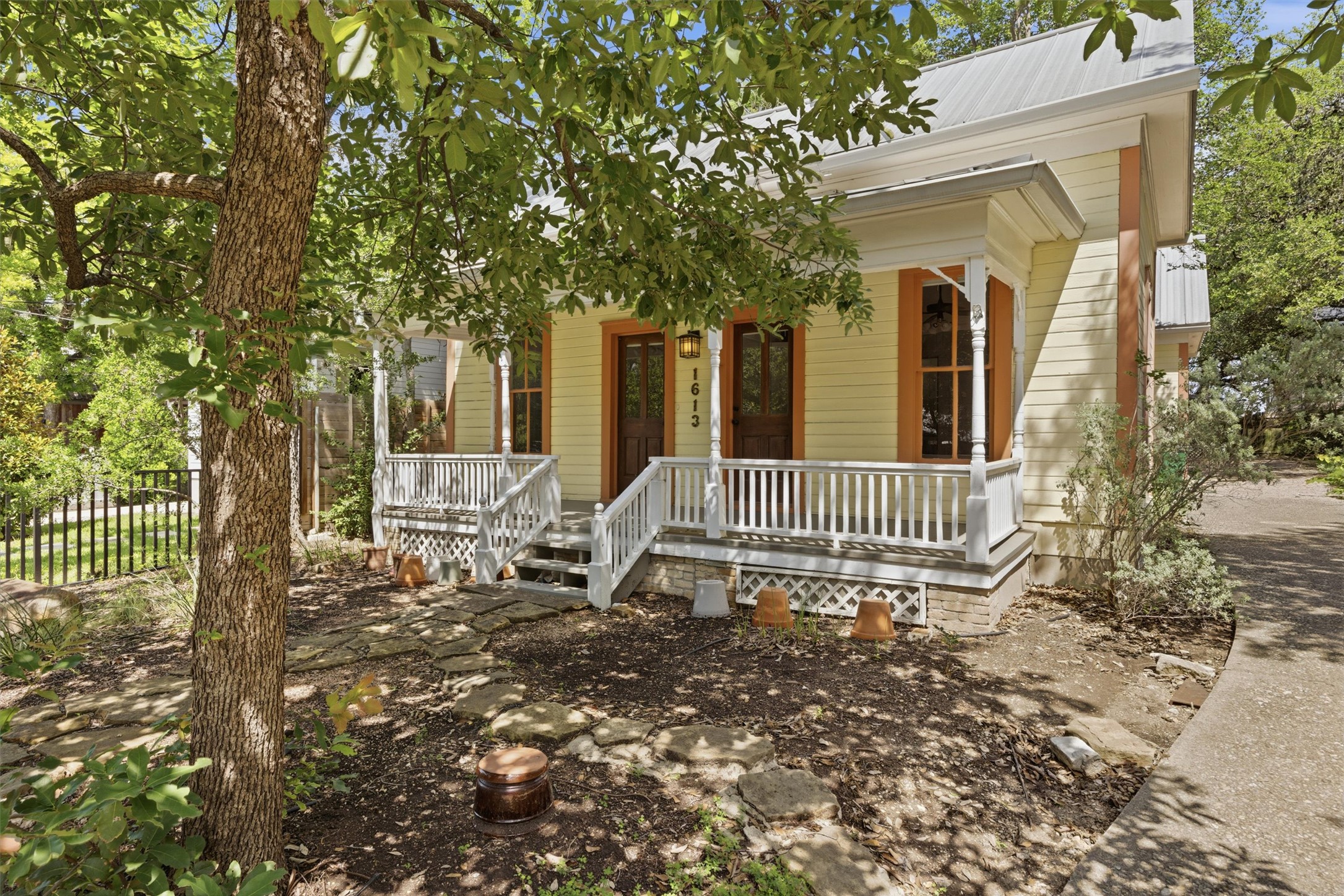 1613 Drake Avenue Austin, TX 78704 - Photo 2 of 27 Light yellow siding exterior with a white metal roof and a covered front porch featuring white railings