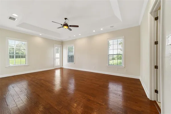 an empty room with wooden floor chandelier fan and windows