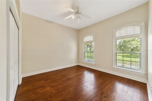 a view of an empty room with wooden floor and a ceiling fan