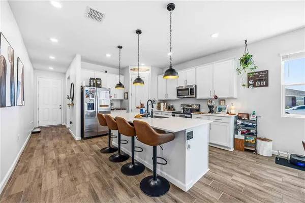 a kitchen with stainless steel appliances kitchen island granite countertop a stove a sink a refrigerator and chairs with wooden floor