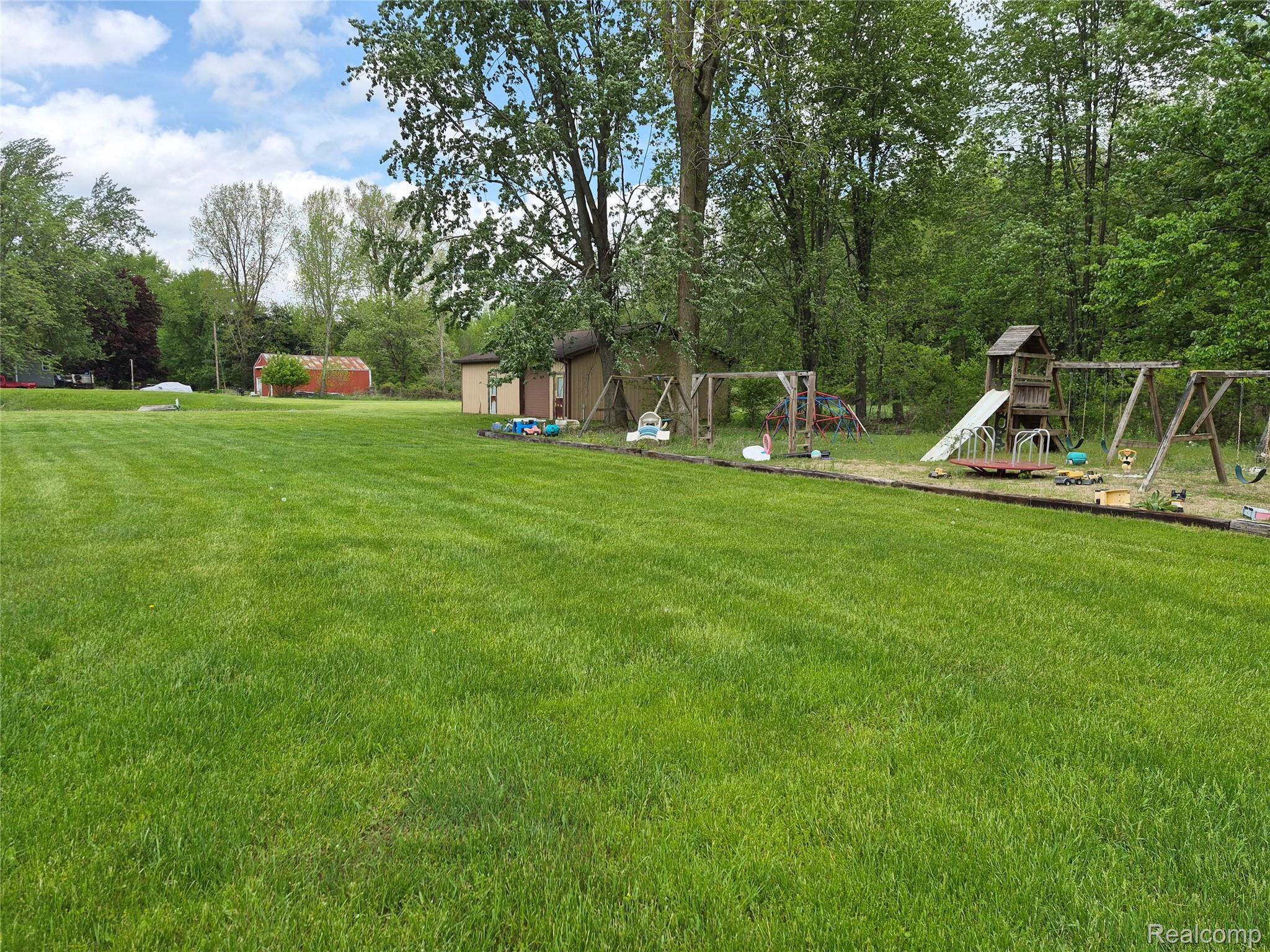 12849 South Delaney Road Perry, MI 48872 - Photo 31 of 34 Expansive green lawn extending towards a wooded area, featuring a detached shed and a red barn structure in the distance