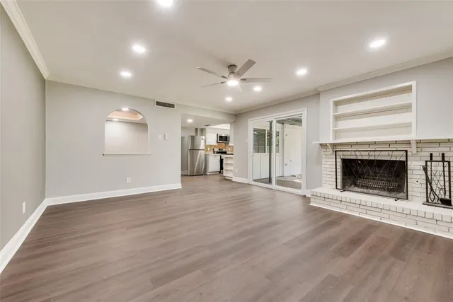 an empty room with wooden floor a fireplace and a kitchen view