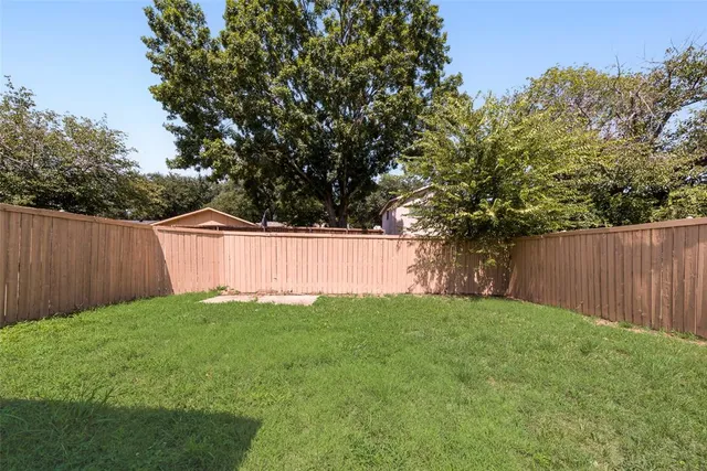 a view of a backyard with large trees and wooden fence