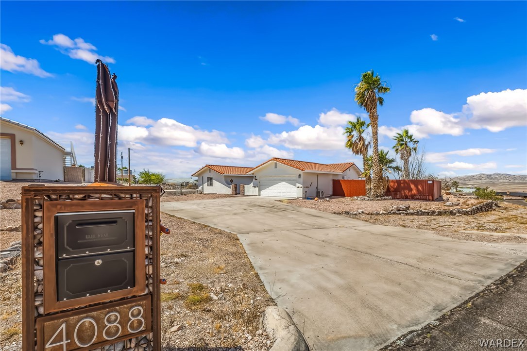 4088 Mercer Road Bullhead City, AZ 86429 - Photo 2 of 35 Property entrance featuring a custom metal mailbox with integrated house numbers, a concrete driveway, and mature palm trees