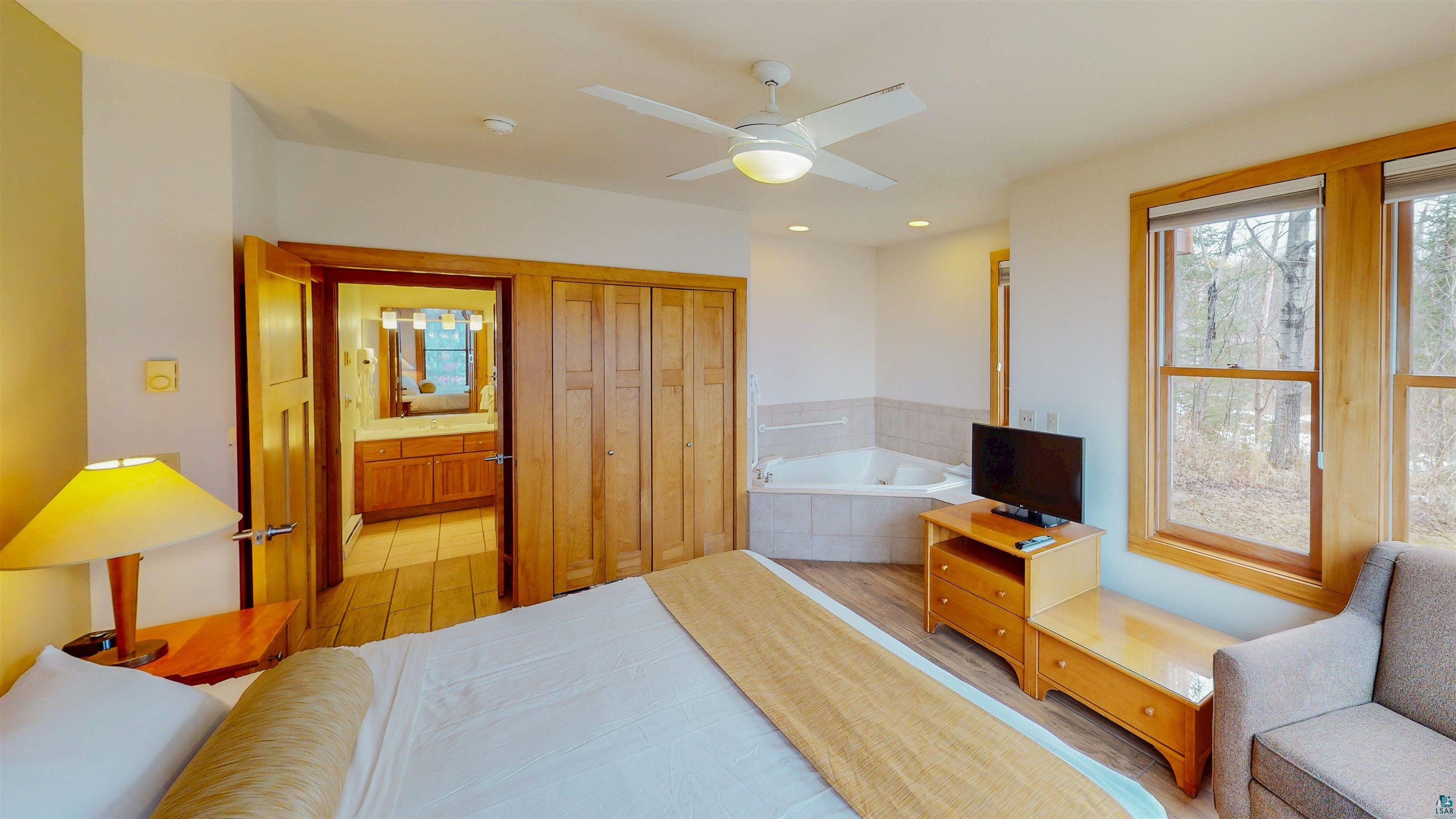 504-506 Poplar River Road, Unit 505 Lutsen, MN 55612 - Photo 12 of 39 Bedroom featuring wood-finish flooring, a ceiling fan with integrated lighting, a built-in jetted tub with tile surround, wood-framed windows, and a doorway to an additional bathroom with a wood vanity