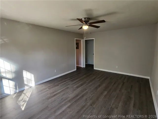 a view of an empty room with wooden floor and a ceiling fan