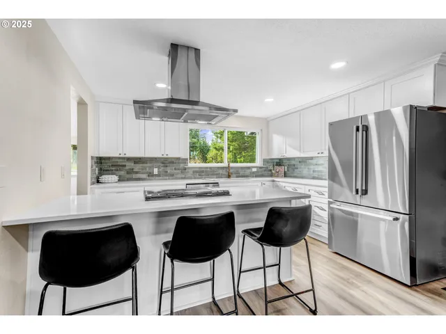 a kitchen with stainless steel appliances a dining table chairs refrigerator and cabinets