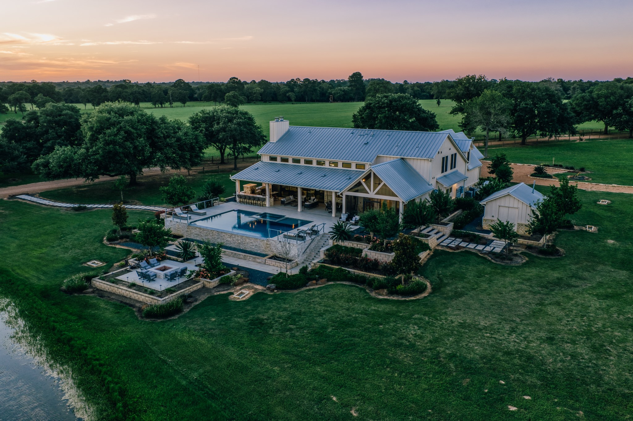 1034 Hilbun Road New Ulm, TX 78950 - Photo 2 of 49 Spectacular waterfront views showcase the custom estate home overlooking a beautifully stocked pond, where illuminated fountains, expansive covered porches, and breathtaking Texas sunsets create an unforgettable setting.