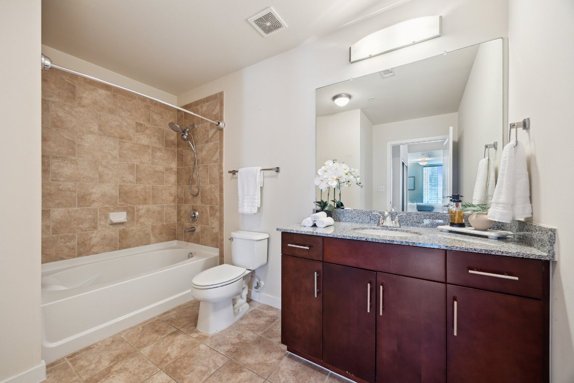 360 Nueces Street, Unit 1116 Austin, TX 78701 - Photo 18 of 33 a bathroom with a granite countertop sink a toilet a mirror a bathtub and shower