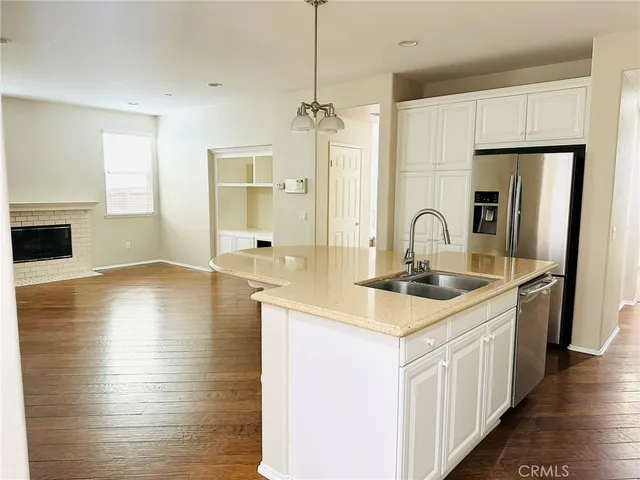 a kitchen with stainless steel appliances a sink dishwasher a refrigerator and white cabinets with wooden floor