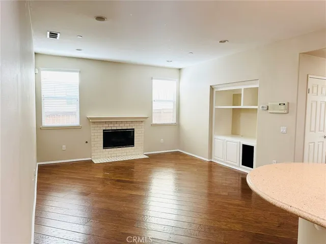 an empty room with wooden floor fireplace and windows