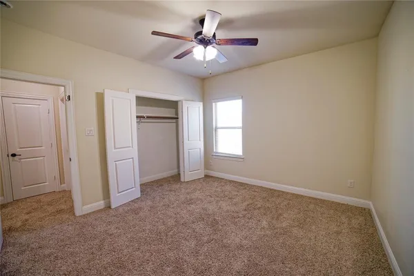 an empty room with chandelier fan and windows