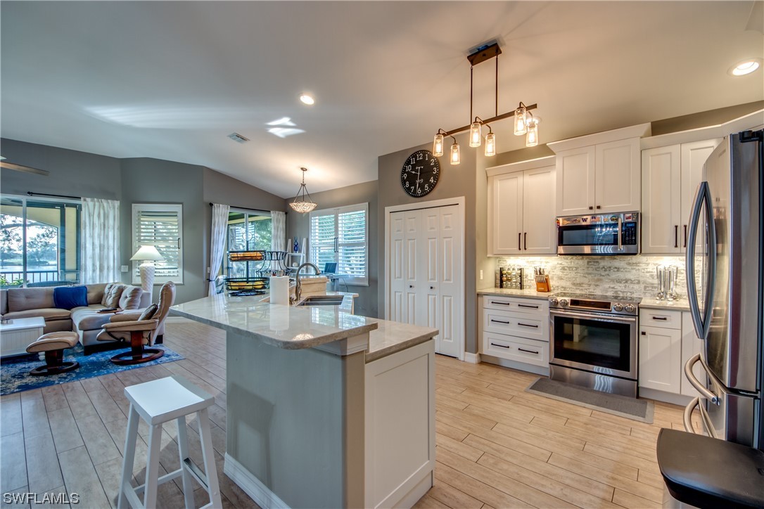 a kitchen with stainless steel appliances kitchen island granite countertop a refrigerator a stove oven a sink dishwasher and white cabinets with wooden floor