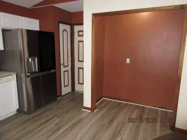 a view of a refrigerator in kitchen and an empty room with wooden floor